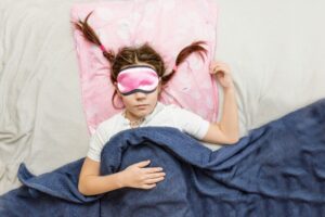 high-grade children's sleep. child girl in a sleep mask sleeps in a bed in a room