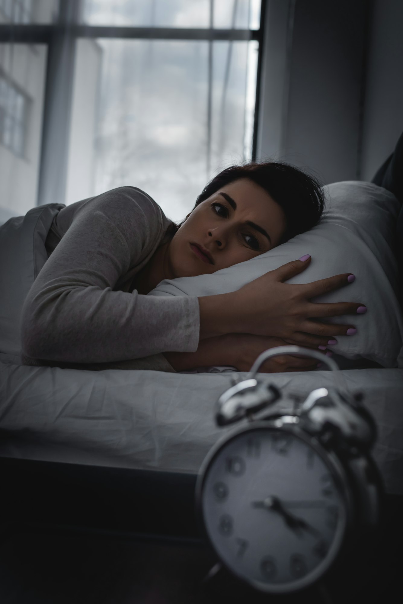 selective focus of awake woman looking at alarm clock on bedside table